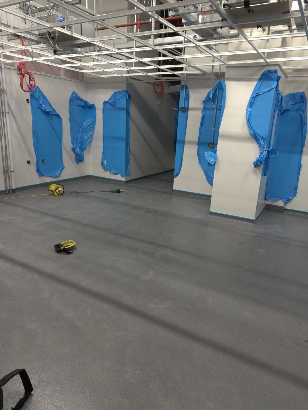 Smooth grey floor across a large open space, with walls masked and protected while work continues