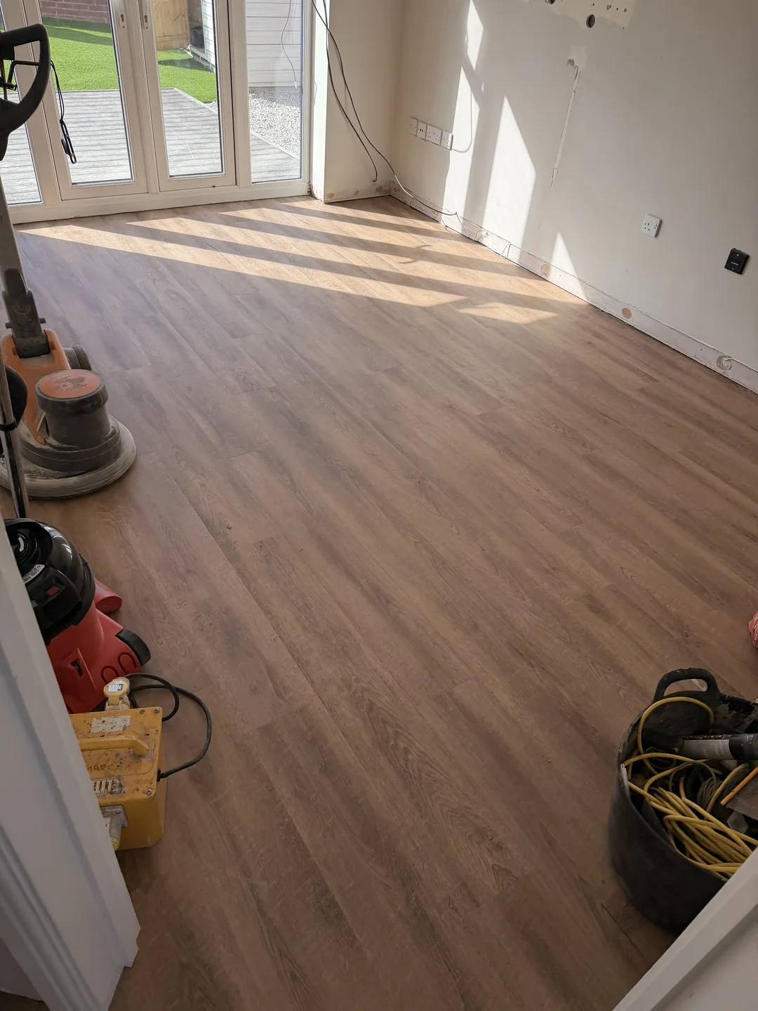 Wood-effect flooring across a sunlit room with equipment at the side