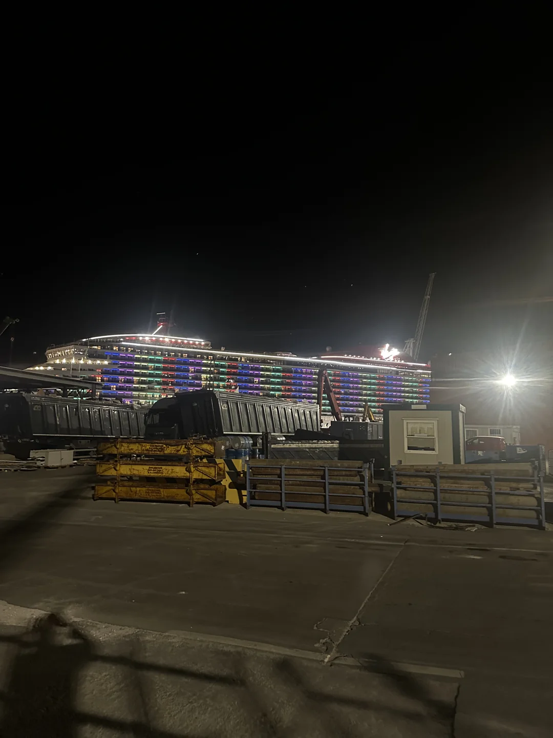 Colourful lights across a ship behind quayside equipment