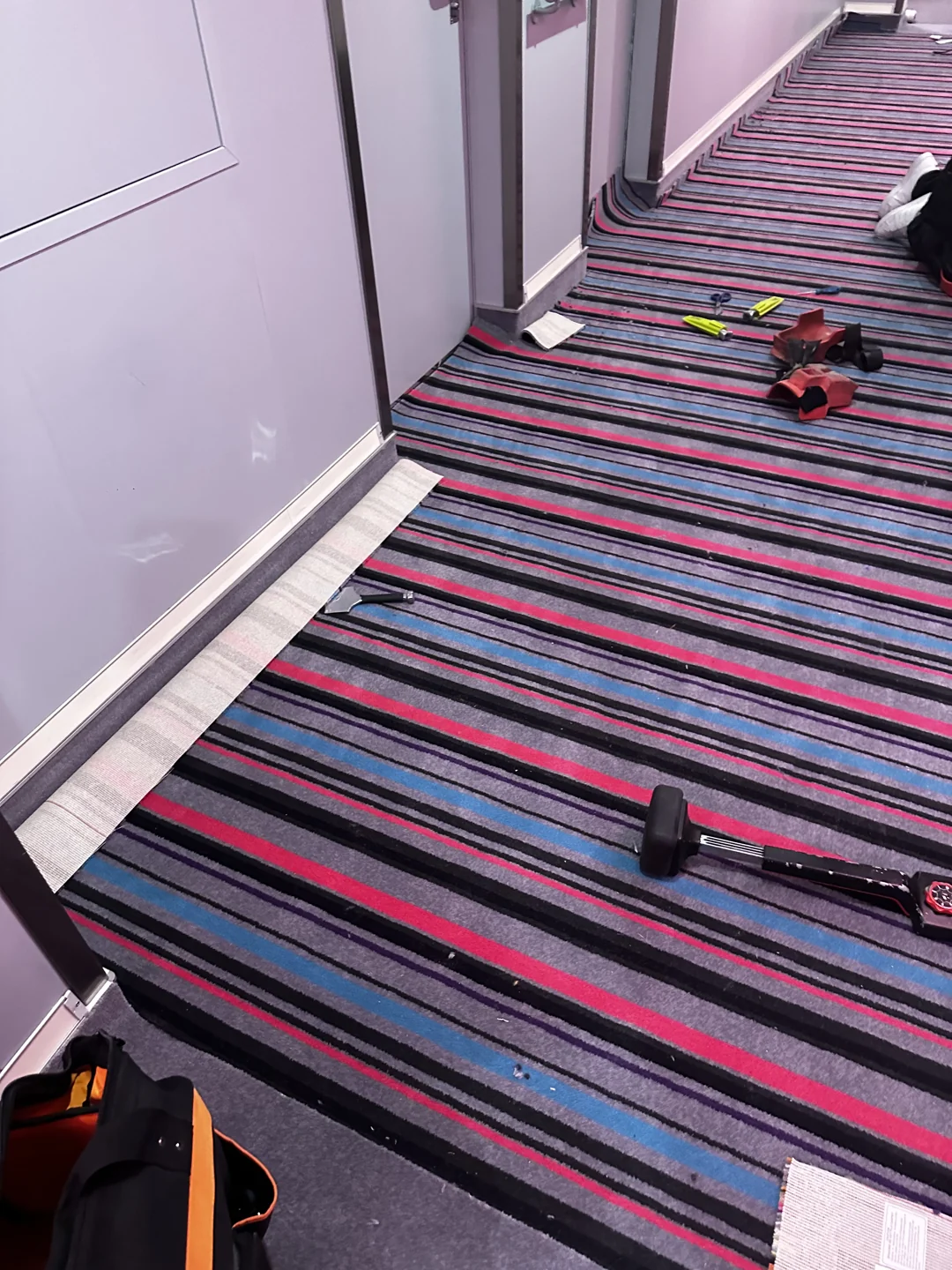 Striped carpet being fitted around corridor doorways with tools visible