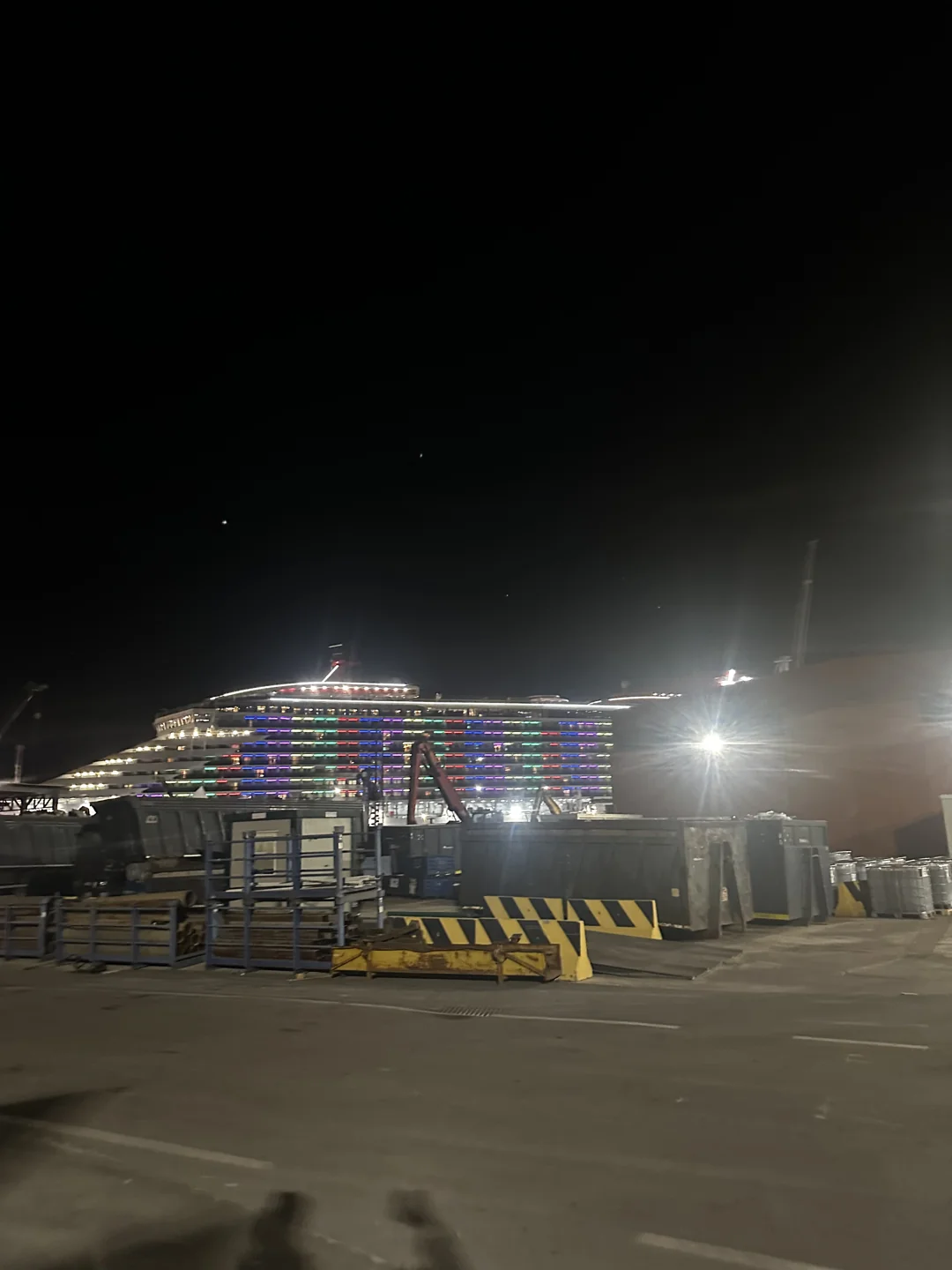 Illuminated ship beyond equipment on the quayside at night
