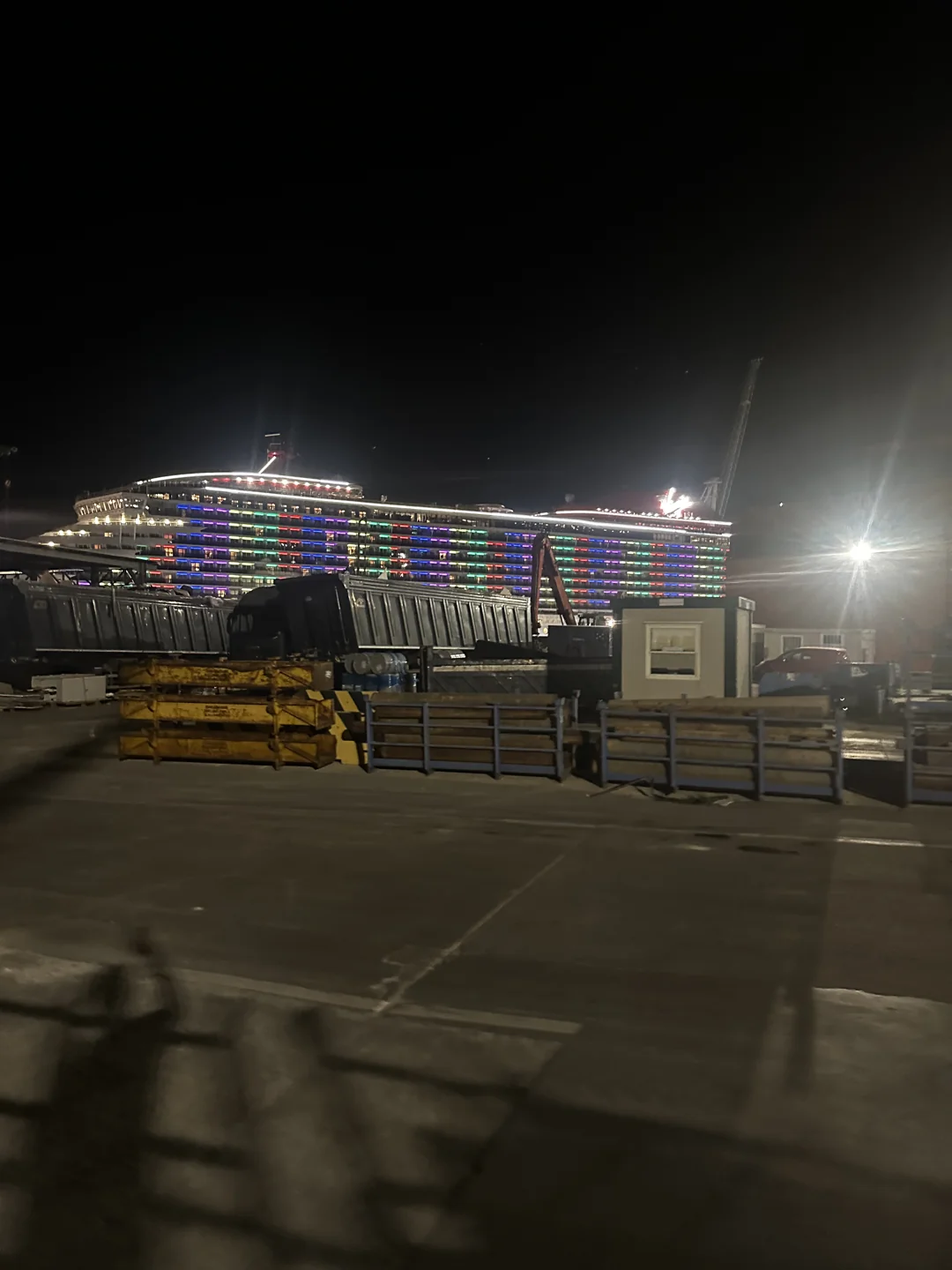 Lit ship behind stacks of quayside equipment