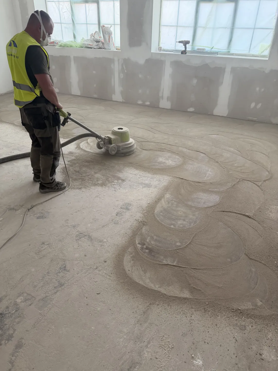 Floor grinding machine in use on a dusty concrete floor beside unfinished walls