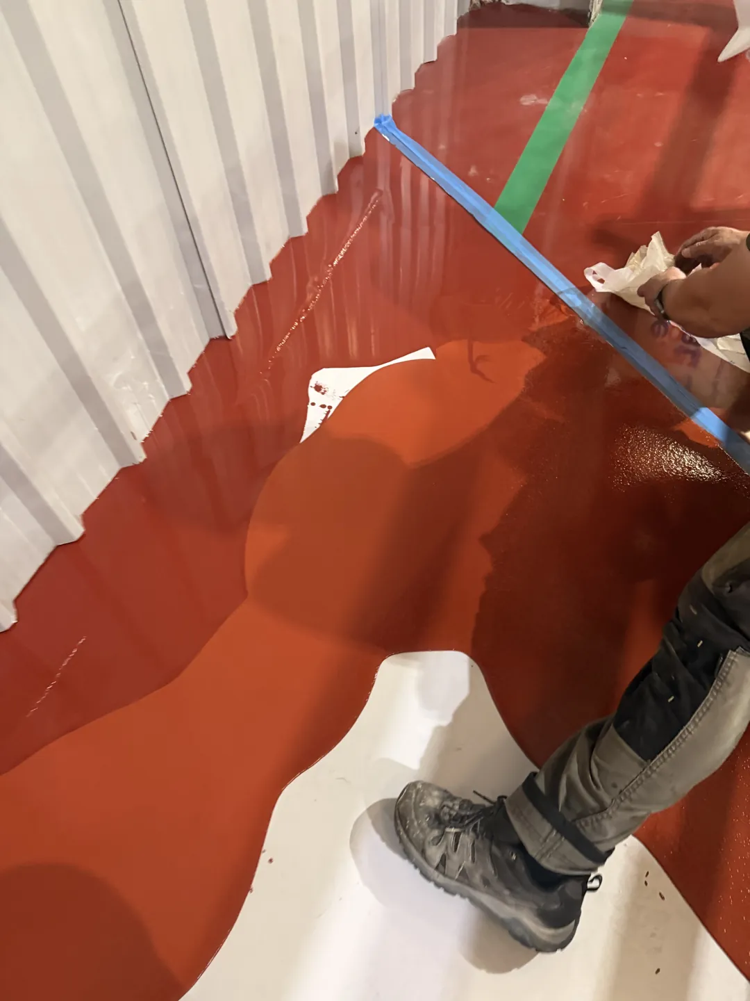 Red floor coating being applied alongside taped edges and a green line